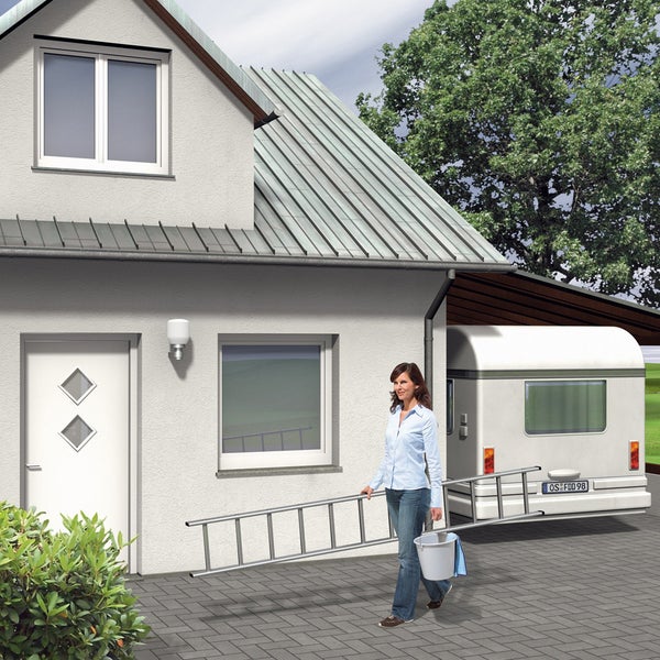 Frau mit Leiter und Eimer vor Haus und Wohnwagen