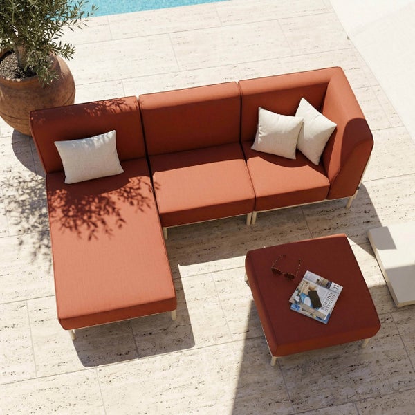 Modulares Garten-Lounge-Set aus terracottafarbenem Stoff mit weißem Gestell, bestehend aus Ecksofa und Hocker auf einer hellen Steinterrasse.