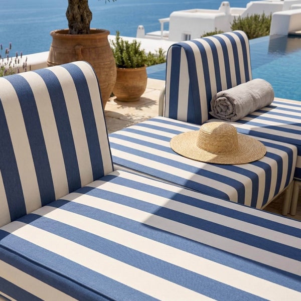Gartenmöbel mit blau und weiß gestreiften Polstern auf einer Terrasse am Pool mit Meerblick.