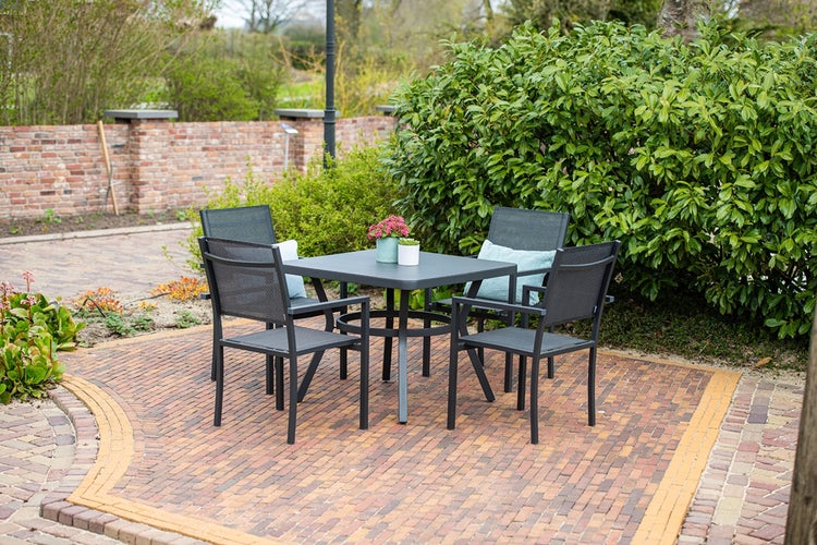 Moderne Gartenmöbel-Garnitur bestehend aus einem quadratischen Tisch und vier Armlehnenstühlen auf einer Terrasse aus Backstein.