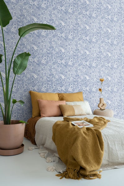 Schlafzimmer mit floral gemusterter Tapete, Bett mit Kissen und Decken sowie Zimmerpflanze