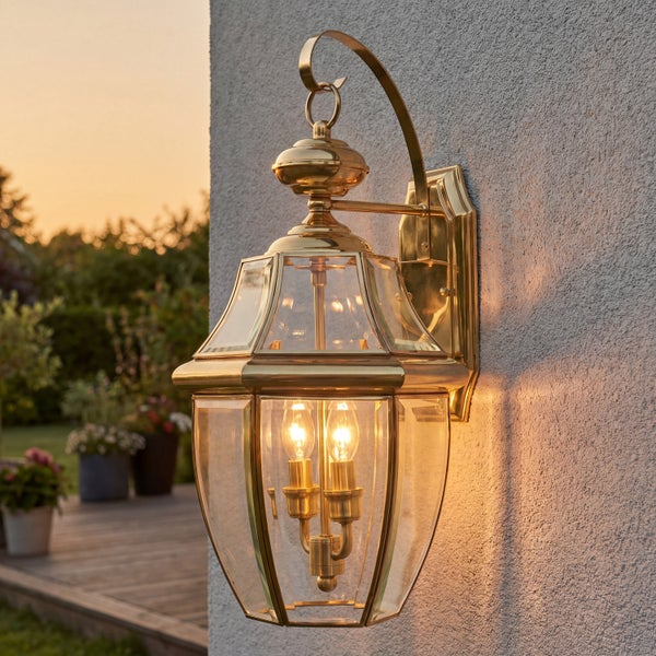 Klassische Außenwandleuchte aus Messing mit klarem Glas und zwei brennenden Kerzenlampen, montiert an einer Hauswand.