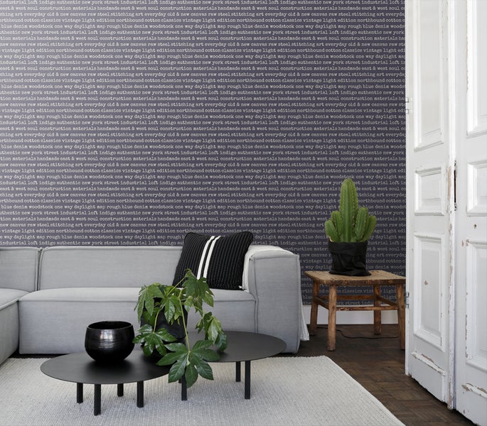 Wohnzimmer mit grauer Couch, Couchtisch, Pflanze und Wandtapete mit Schriftzug