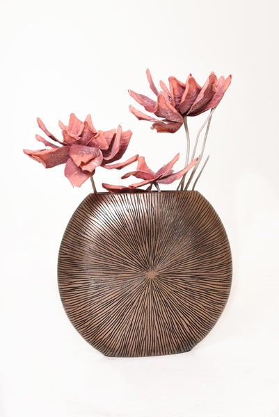 Dekorative runde Vase in Bronzeoptik mit strahlenförmiger Struktur und künstlichen korallenfarbenen Trockenblumen.