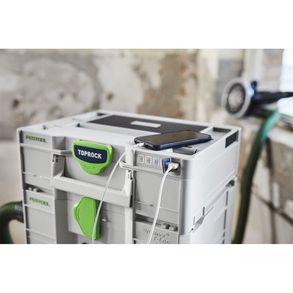 Festool TOPROCK Bluetooth-Lautsprecher im Systainer auf einer Baustelle, ein Smartphone wird über den integrierten USB-Anschluss geladen.