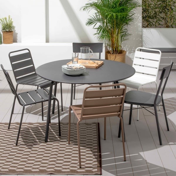 Heller Terrassenbereich mit einem runden, anthrazitfarbenen Metalltisch, verschiedenen Gartenstühlen und einem gemusterten Außenteppich.