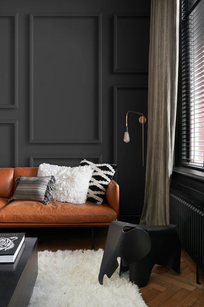 Wohnzimmer mit Ledersofa, Zierkissen, Teppich und Dekorationshocker in Elefantenform.