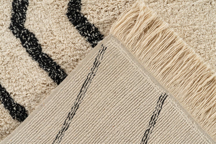 Nahaufnahme eines Hochflor-Teppichs mit schwarzen Wellenmustern und langen Fransen, Ansicht von weicher Oberseite und gewebter Rückseite.