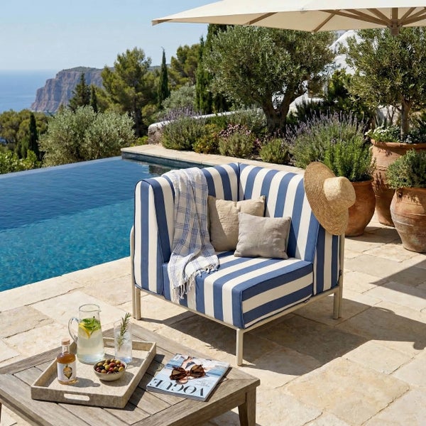 Helle Außenterrasse mit blau-weiß gestreiftem Sessel, Swimmingpool, Natursteinplatten und Holztisch.