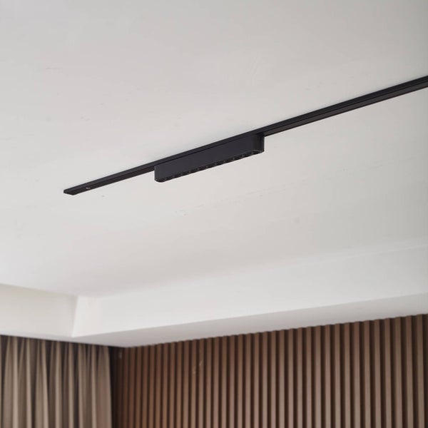 Schwarzer linearer Schienenstrahler an einer schwarzen Schiene an der Decke eines modernen Raumes mit Holzpaneelen.