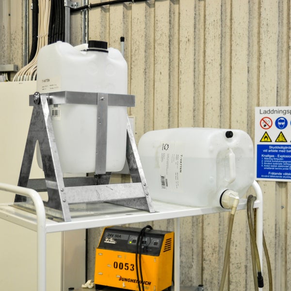 Zwei Wasserkanister auf einem Regal mit einem Batterieladegerät im Hintergrund.