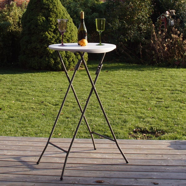 Ein runder, klappbarer Stehtisch mit Metallgestell steht auf einer Holzterrasse im Garten, dekoriert mit einer Flasche und zwei Gläsern.