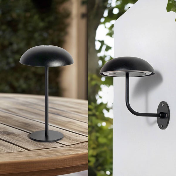 Moderne schwarze Außenleuchte in Pilzform als Tischlampe auf einem Holztisch und als Wandlampe an einer weißen Wand.