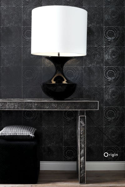 Szene mit Tisch, Lampe und gepolstertem Hocker vor einer Wand mit quadratischer Holzscheiben-Tapete