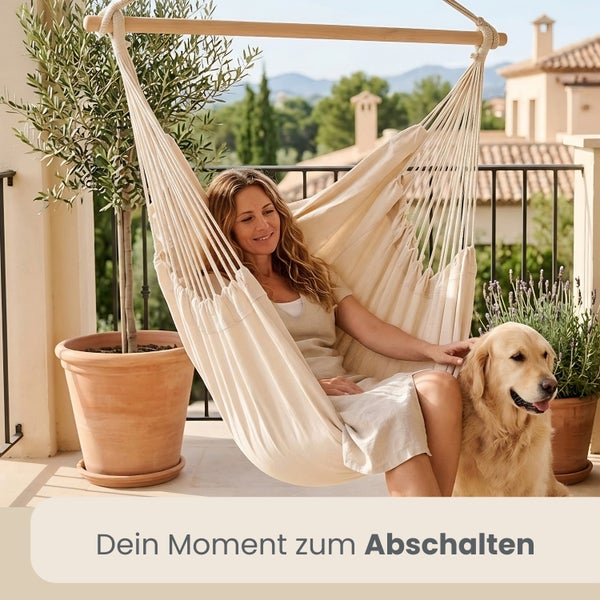 Frau in beigem Hängesessel auf hellem Balkon mit Golden Retriever, Olivenbaum im Terrakotta-Topf und Lavendel im Hintergrund.