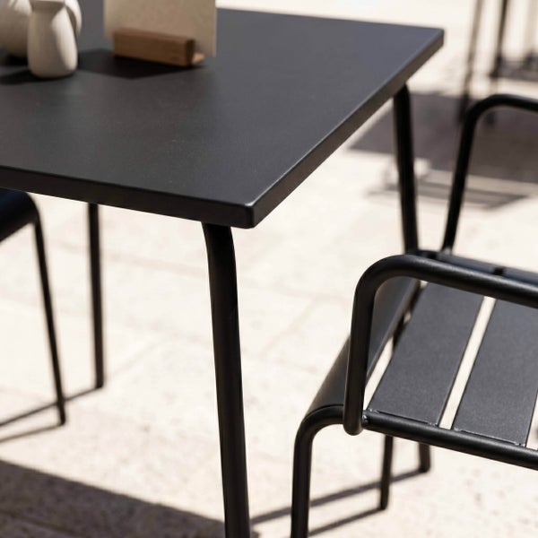 Modernes Gartenmöbel Set bestehend aus einem schwarzen Metalltisch und einem passenden Armlehnenstuhl mit Latten auf einer hellen Terrasse.