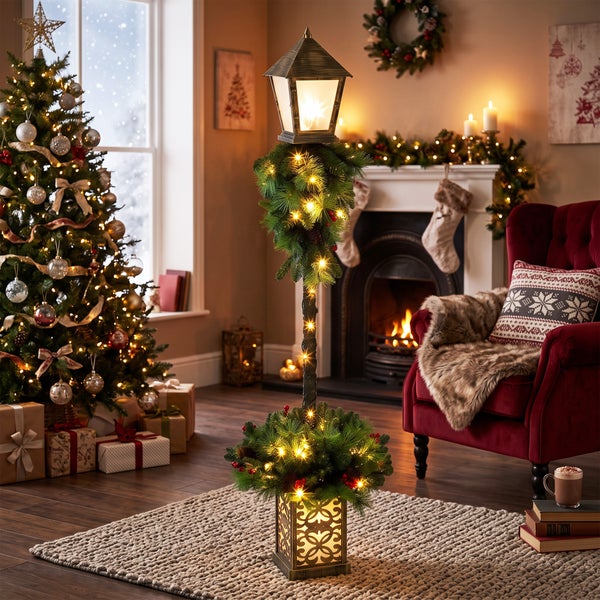 Beleuchtete Weihnachtsdekoration in Form einer Laterne mit Tannenbaumoptik, Lichtern und Tannenzweigen in einem festlich dekorierten Wohnzimmer.