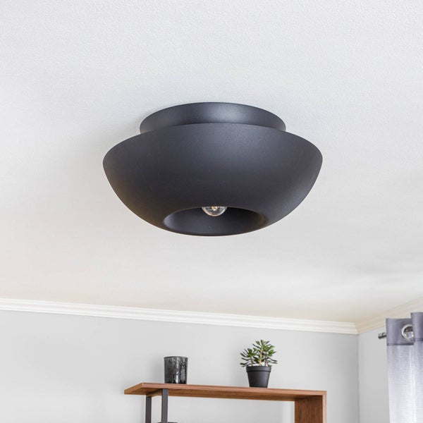 Moderne schwarze Deckenleuchte in runder Schalenform an einer Zimmerdecke über einem Holzregal mit Pflanze.