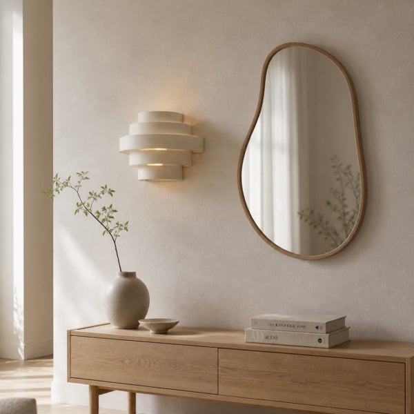 Ein moderner Wohnbereich mit einem organisch geformten Wandspiegel, einer geschichteten Wandleuchte und einem hölzernen Sideboard.