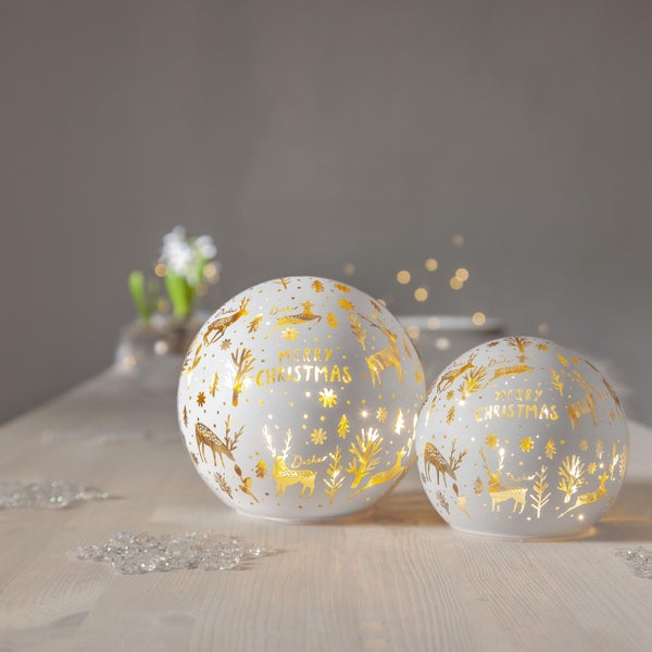 Zwei weihnachtliche Kugellampen mit Rentier- und Weihnachtsbaummotiven auf einem Tisch