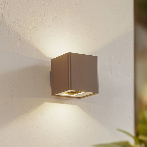 Braune, würfelförmige Außenwandleuchte mit Lichtaustritt nach oben und unten an einer Wand.