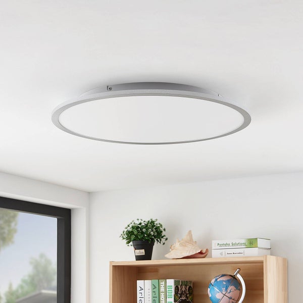 Runde, flache LED-Deckenleuchte an einer weißen Zimmerdecke über einem Holzregal in einem hellen Raum.