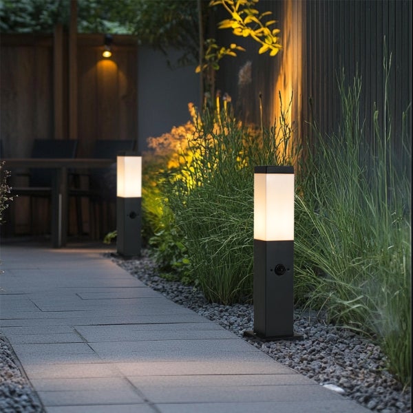 Moderne schwarze LED-Wegeleuchte in einem Garten mit Kies und Pflanzen neben einem gepflasterten Weg.