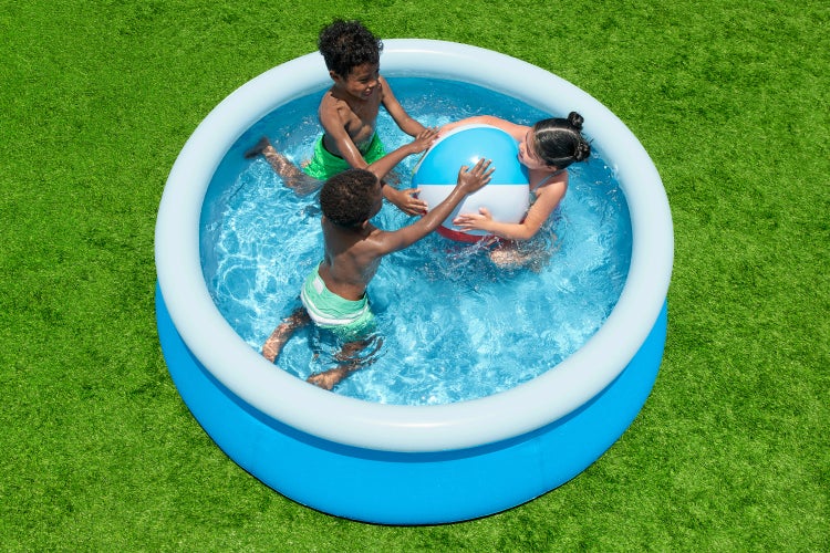 Drei Kinder spielen mit einem großen Wasserball in einem runden, aufblasbaren Planschbecken auf einer Rasenfläche.