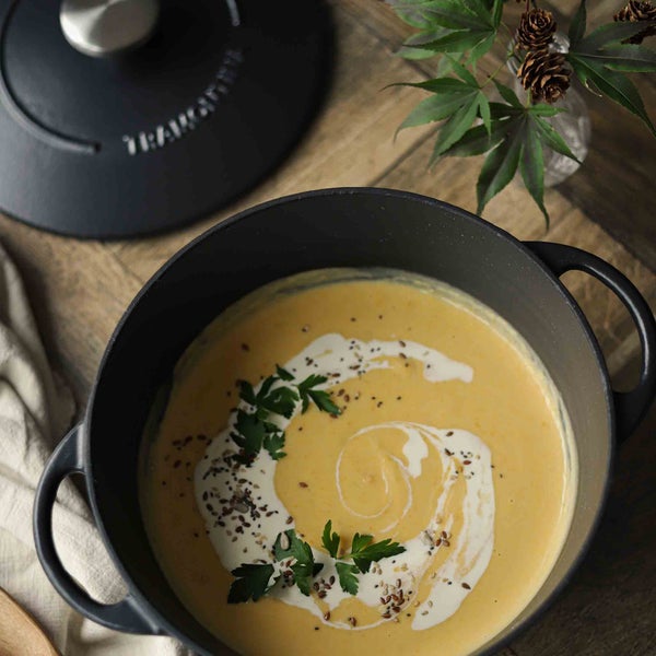 Topf mit Kürbissuppe, garniert mit Sahne und Kräutern auf einem Holztisch
