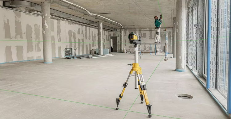 Stabila Kreuzlinienlaser auf einem Stativ in einer Baustelle, während ein Handwerker auf einem Gerüst an der Decke arbeitet.