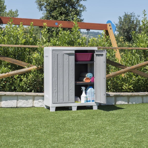Grauer Gartenschrank mit geöffneter Tür, gefüllt mit Reinigungsutensilien und Handtüchern, steht im Garten.