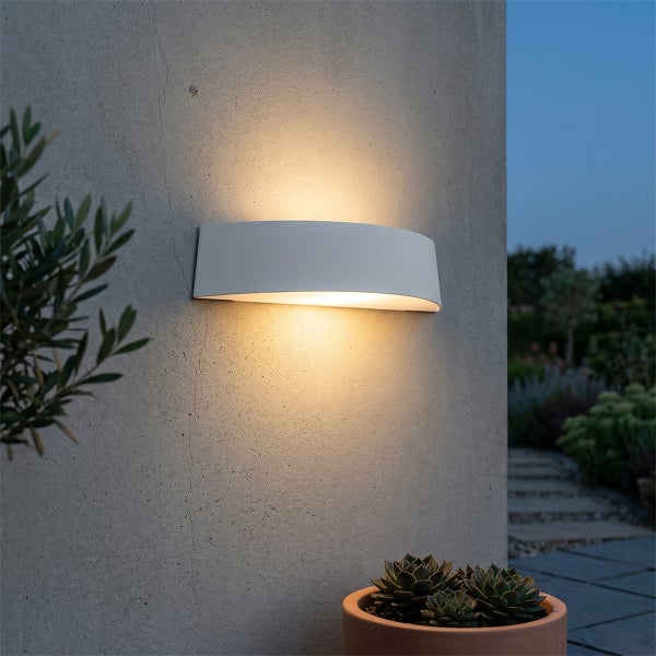Moderne weiße Außenwandleuchte mit Lichtaustritt nach oben und unten an einer Betonwand im Garten bei Dämmerung.