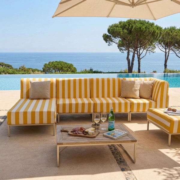 Modernes Lounge-Set auf einer Terrasse am Pool mit gelb-weiß gestreiftem Sofa, passendem Hocker und Holztisch mit Meerblick.