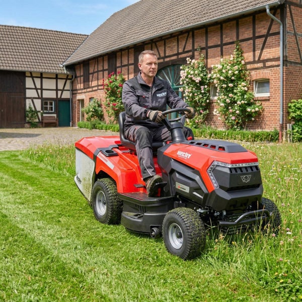 Mann fährt einen Rasentraktor der Marke Hecht in einem Garten vor einem Haus.