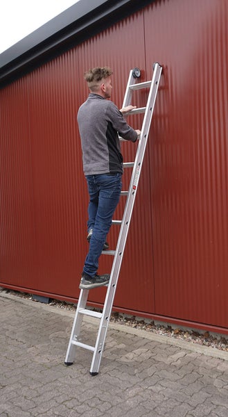 Mann auf einer Aluminium-Anlegeleiter vor einer Wand