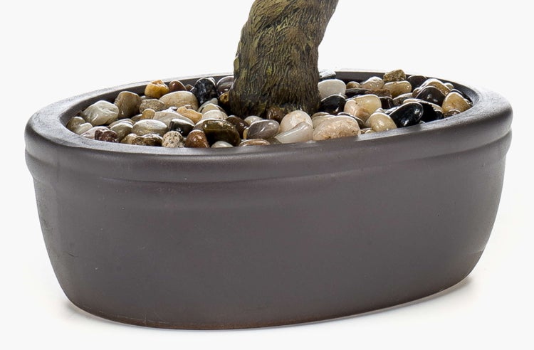Künstlicher Bonsai im dunklen Topf mit grünen Nadelblättern und Kieselsteinen.