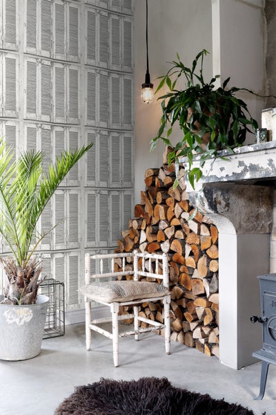 Wohnzimmer mit Kamin, Holzstapel, Stuhl und Tapete im Fensterladen-Design