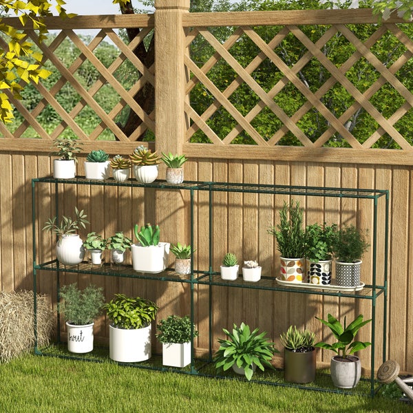 Dunkelgrünes Pflanzenregal aus Metall mit drei Ebenen vor einem Holzzaun im Garten, bestückt mit verschiedenen Topfpflanzen.