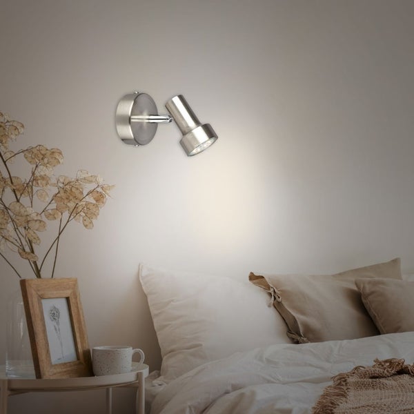 Verstellbarer Wandstrahler aus Metall über einem Bett in einem modern eingerichteten Schlafzimmer.