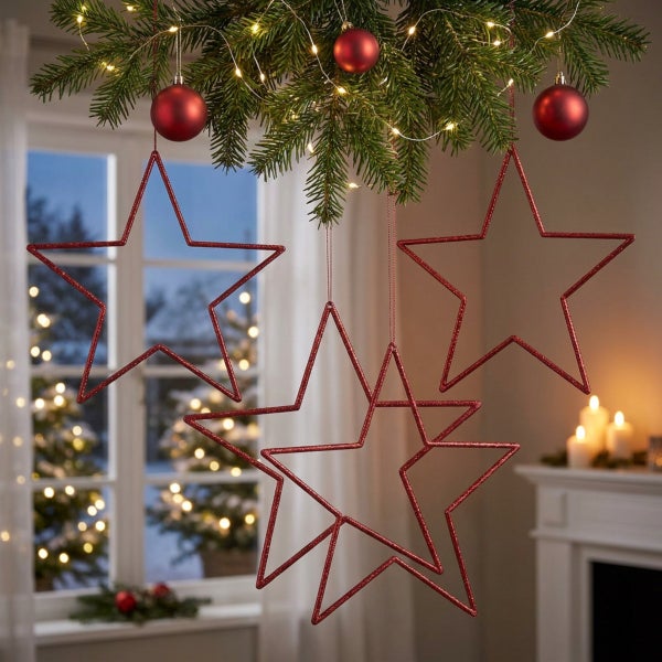 Drei hängende Weihnachtssterne aus Metall als Fensterdekoration in einem festlich dekorierten Wohnzimmer mit Tannenbaumzweigen.