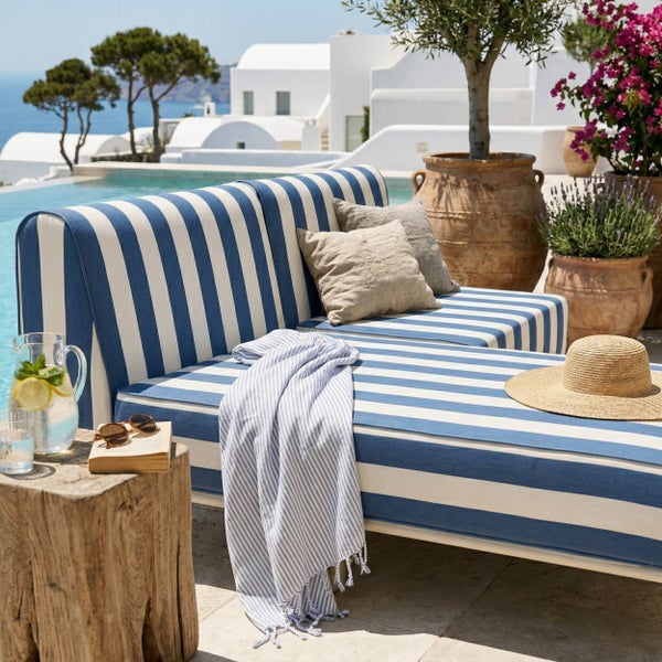 Blau und weiß gestreifte Gartenlounge mit Kissen und Decke auf einer hellen Terrasse am Pool in mediterranem Ambiente.