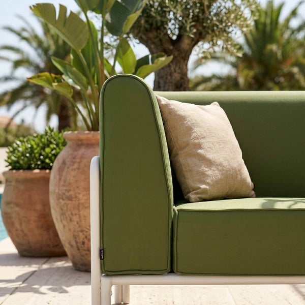 Grünes Gartensofa mit hellem Dekokissen auf einer Terrasse neben großen Pflanzgefäßen aus Terrakotta.
