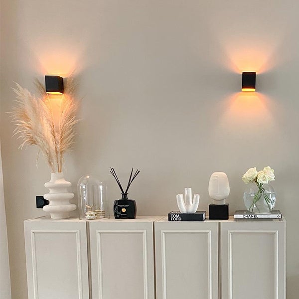 Dekoratives Sideboard mit zwei Wandleuchten und verschiedenen Dekorationsartikeln.