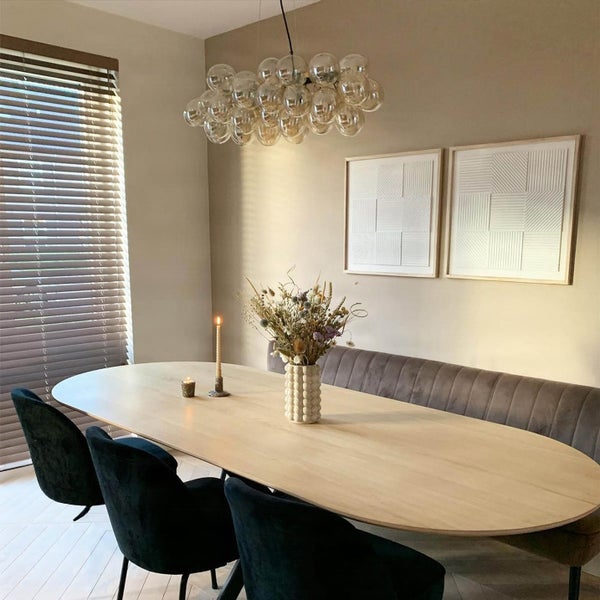 Esszimmer mit ovalem Holztisch, samtiger Sitzbank und schwarzen Stühlen, beleuchtet durch eine moderne Kugelleuchte, stilvolles Interieur Design.