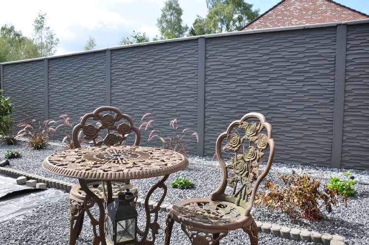 Gartenszene mit einem Tisch und zwei Stühlen vor einem grauen Betonsichtschutzzaun