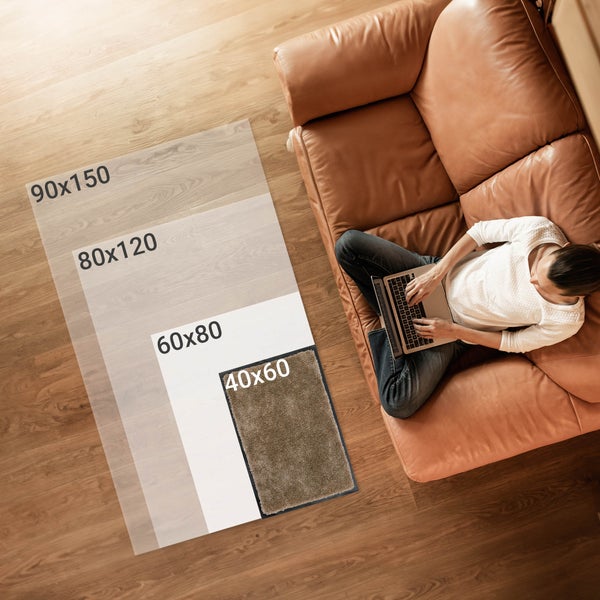 Darstellung verschiedener Teppichgrößen auf einem Boden, daneben sitzt eine Person mit einem Laptop auf einem Sofa.