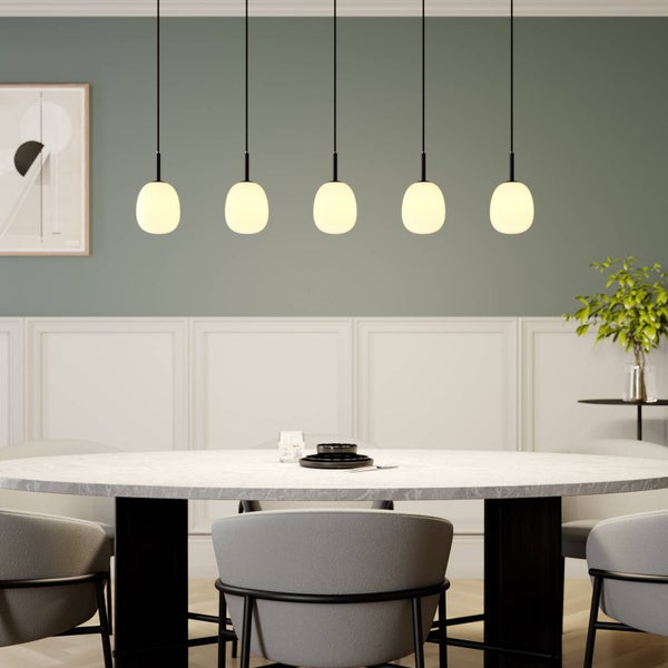 Fünf moderne Pendelleuchten mit ovalen Schirmen aus Opalglas über einem runden Marmortisch in einem hellen Esszimmer.