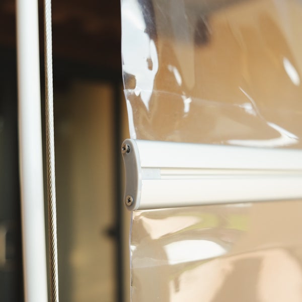 Detailansicht eines transparenten PVC-Wetterschutzrollos mit Aluminium-Abschlussleiste und seitlicher Seilführung aus Edelstahl.