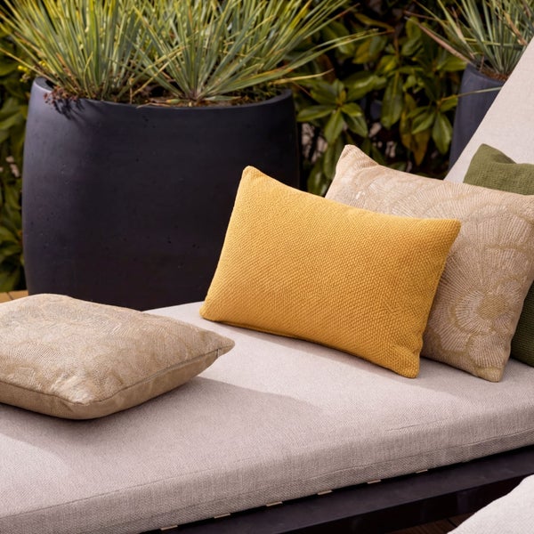 Dekorative Kissen auf einer Gartenliege mit Pflanzgefäßen im Hintergrund.
