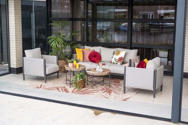 Loungemöbel Set mit hellgrauen Polstern, dunkelgrauem Metallrahmen, Sofa, zwei Sesseln und runden Tischen auf einem gemusterten Außenteppich.